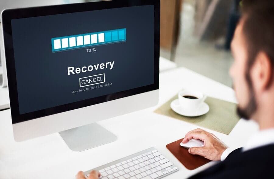 A man sits at a desk, viewing a recovery progress bar on a computer screen, showing 70% completion. A man sits at a desk, viewing a recovery progress bar on a computer screen, showing 70% completion.