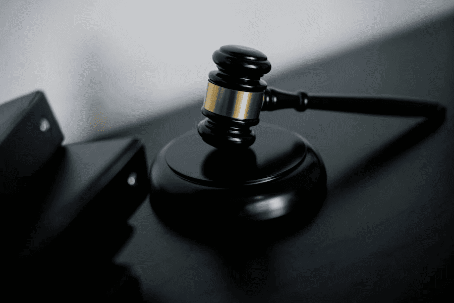 A wooden judge's gavel with a golden band rests on a sound block on a dark surface. Nearby are closed black folders, conveying a legal theme. A wooden judge's gavel with a golden band rests on a sound block on a dark surface. Nearby are closed black folders, conveying a legal theme.